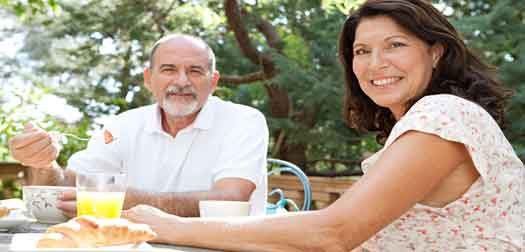 couple-eatting Portrait of a senior couple enjoying a healthy breakfast together in a luxury home garden on holiday. Mature people eating healthy food and enjoying each others company, smiling outdoors. Travel lifestyle.